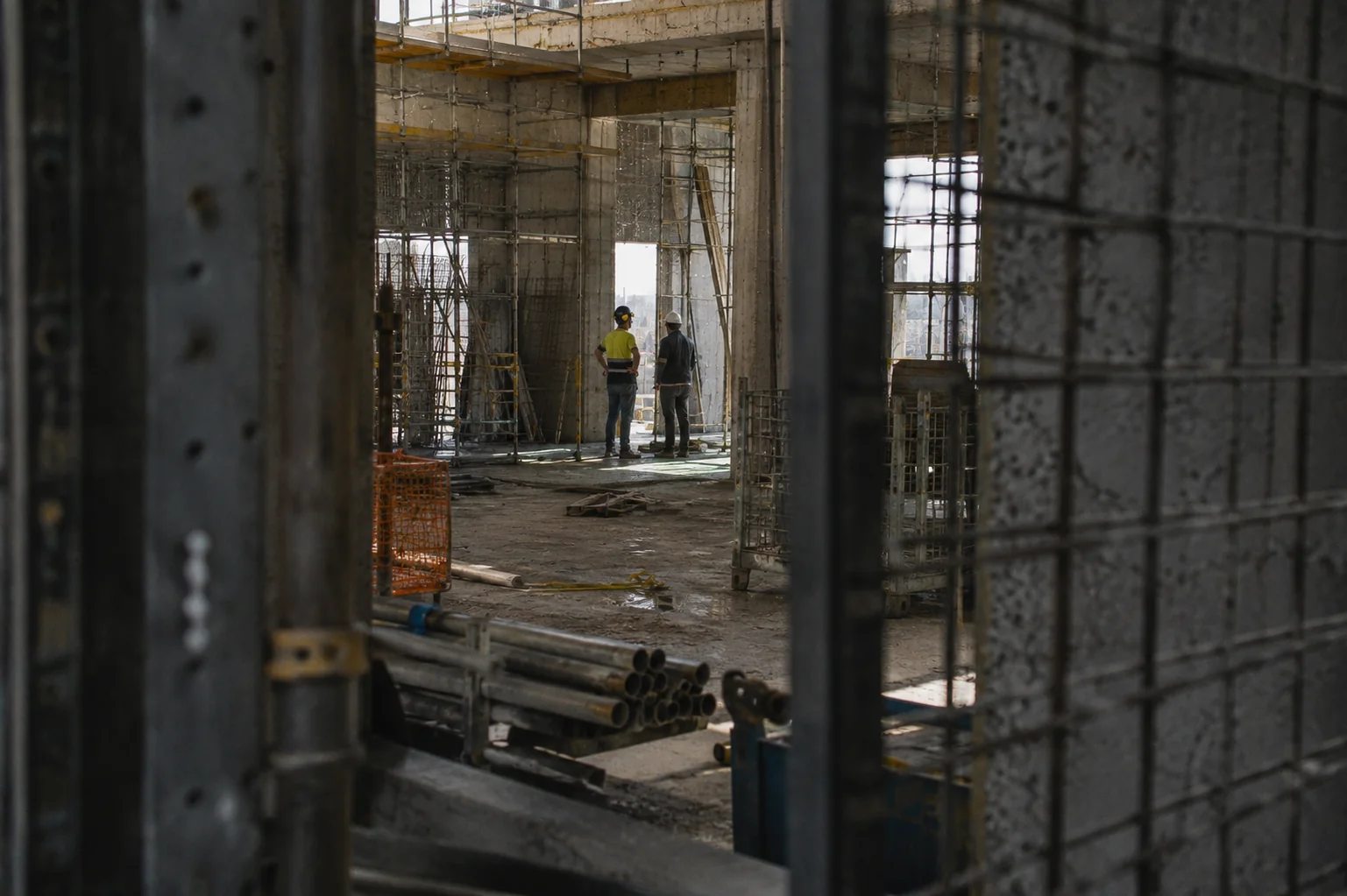 Obra activa vista desde la distancia con dos técnicos coordinándose entre estructura y andamios.